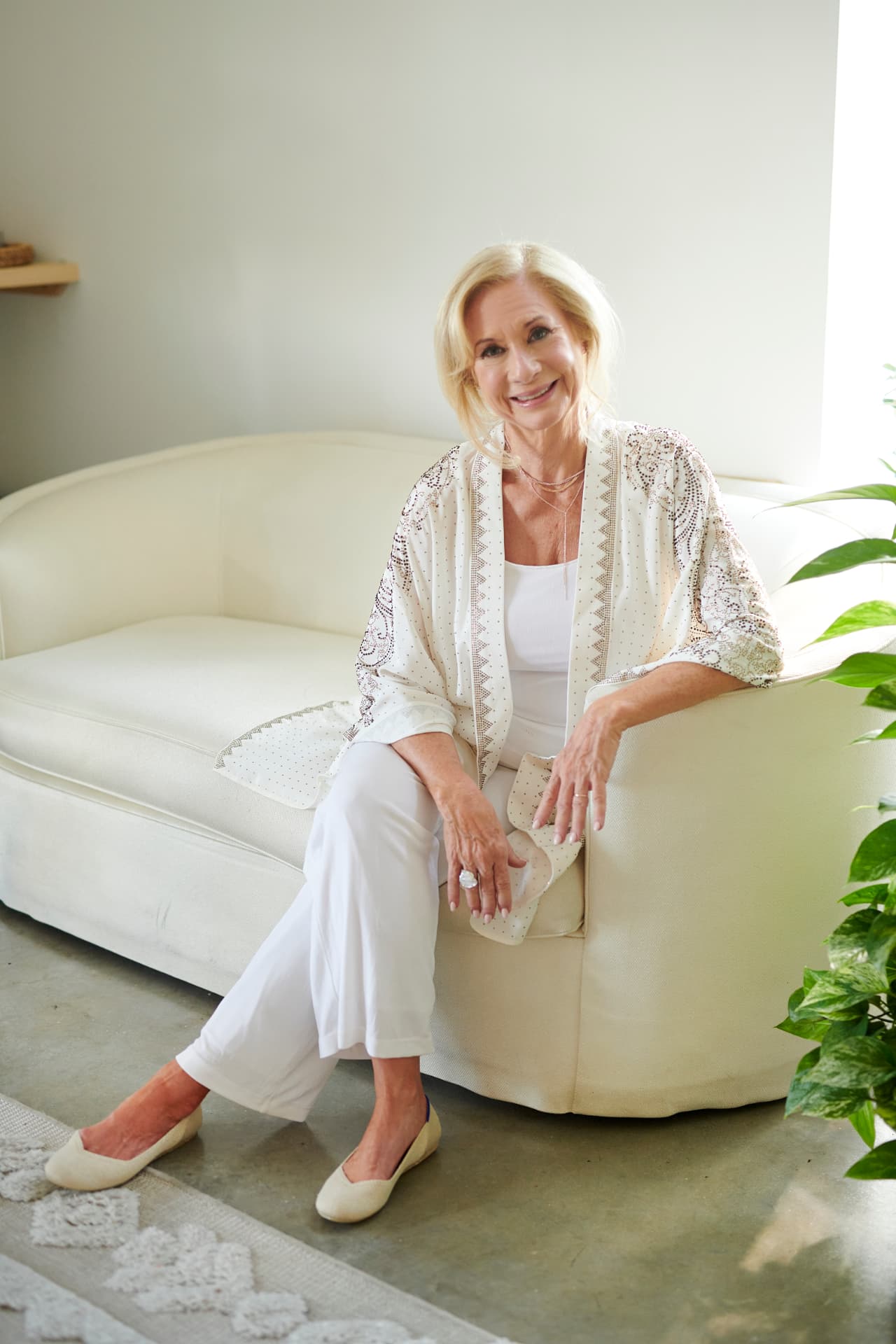 Jennifer seated on a cream sofa in white, smiling warmly