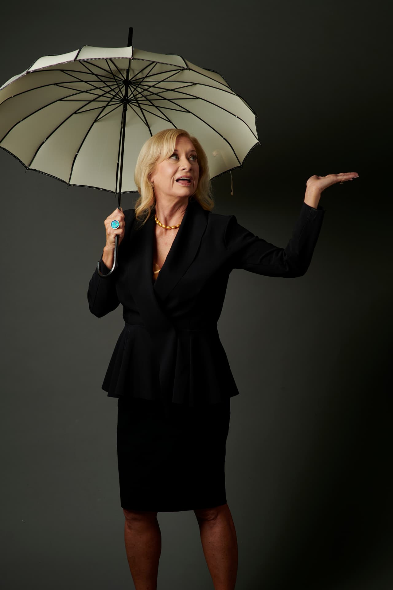 Jennifer holding a cream umbrella, hand out to feel the rain
