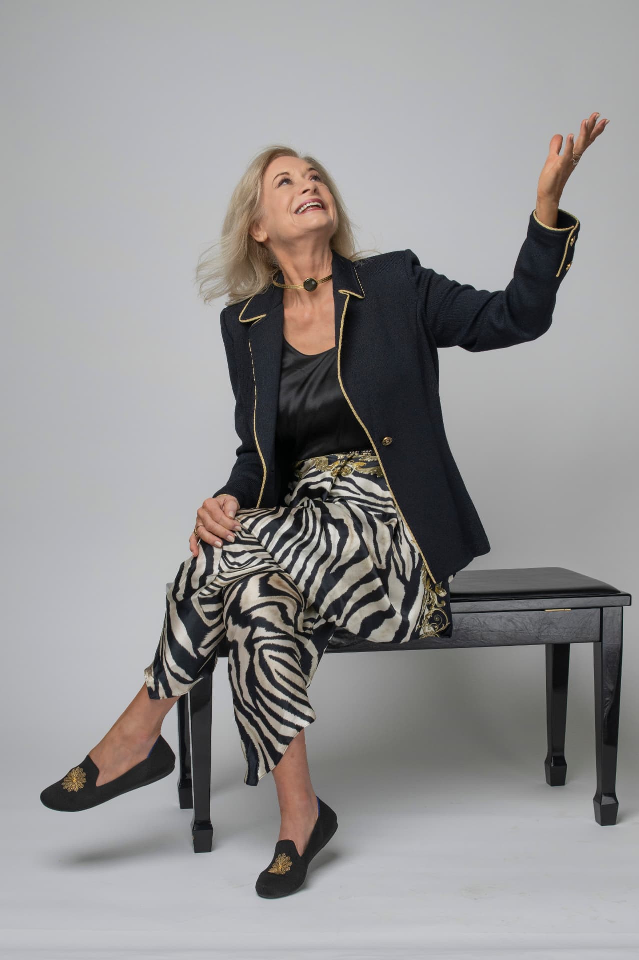 Jennifer laughing with one arm raised, seated on a bench in a navy blazer